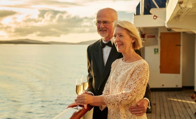 A couple on the Promenade Deck on the Hebridean Princess cruise ship of Hebridean Island Cruises with glasses of champagne