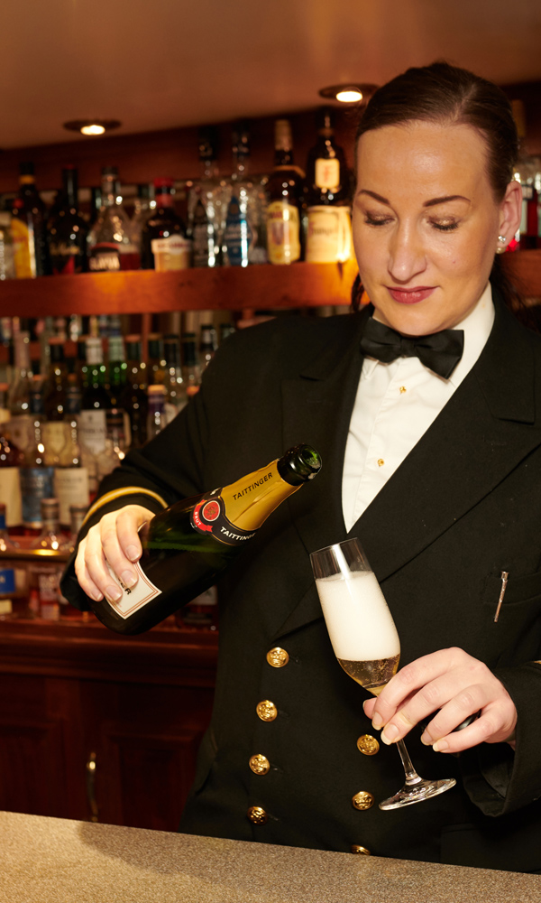 A female crew member on the Hebridean Princess cruise ship pouring a drink in the Tiree Lounge