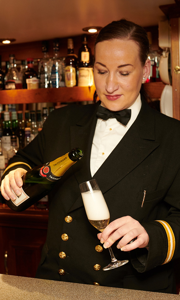 A crew member on Hebridean Princess cruise ship pouring a drink in the Tiree Lounge