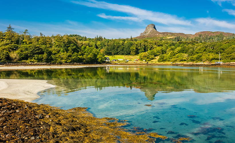 A stunning bay with crystal blue waters on the Isle of Eigg on a sunny day with An Sgurr in the background