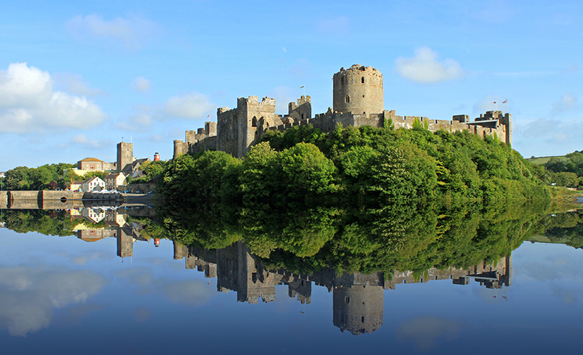 Pembroke Castle in Wales with the castle reflecting off the calm water