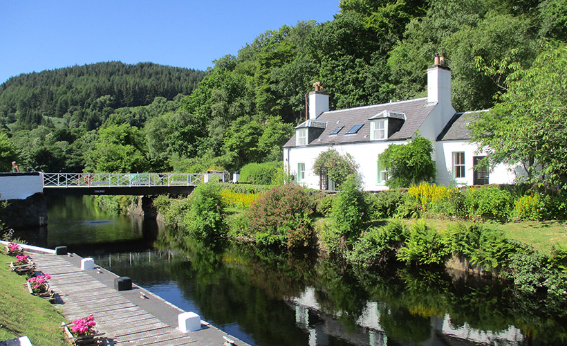 The Crinan Canal on a sunny day with a cottage nestled on its banks