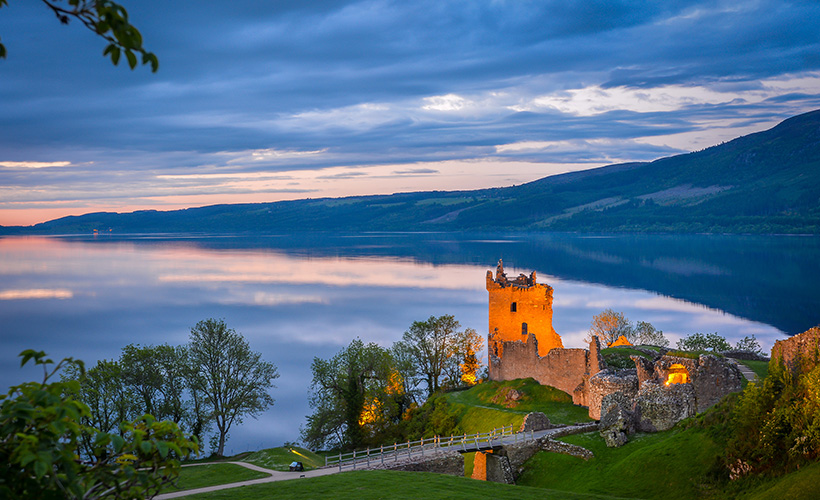 Urquhart Castle lit up in the evening with Loch Ness in the background